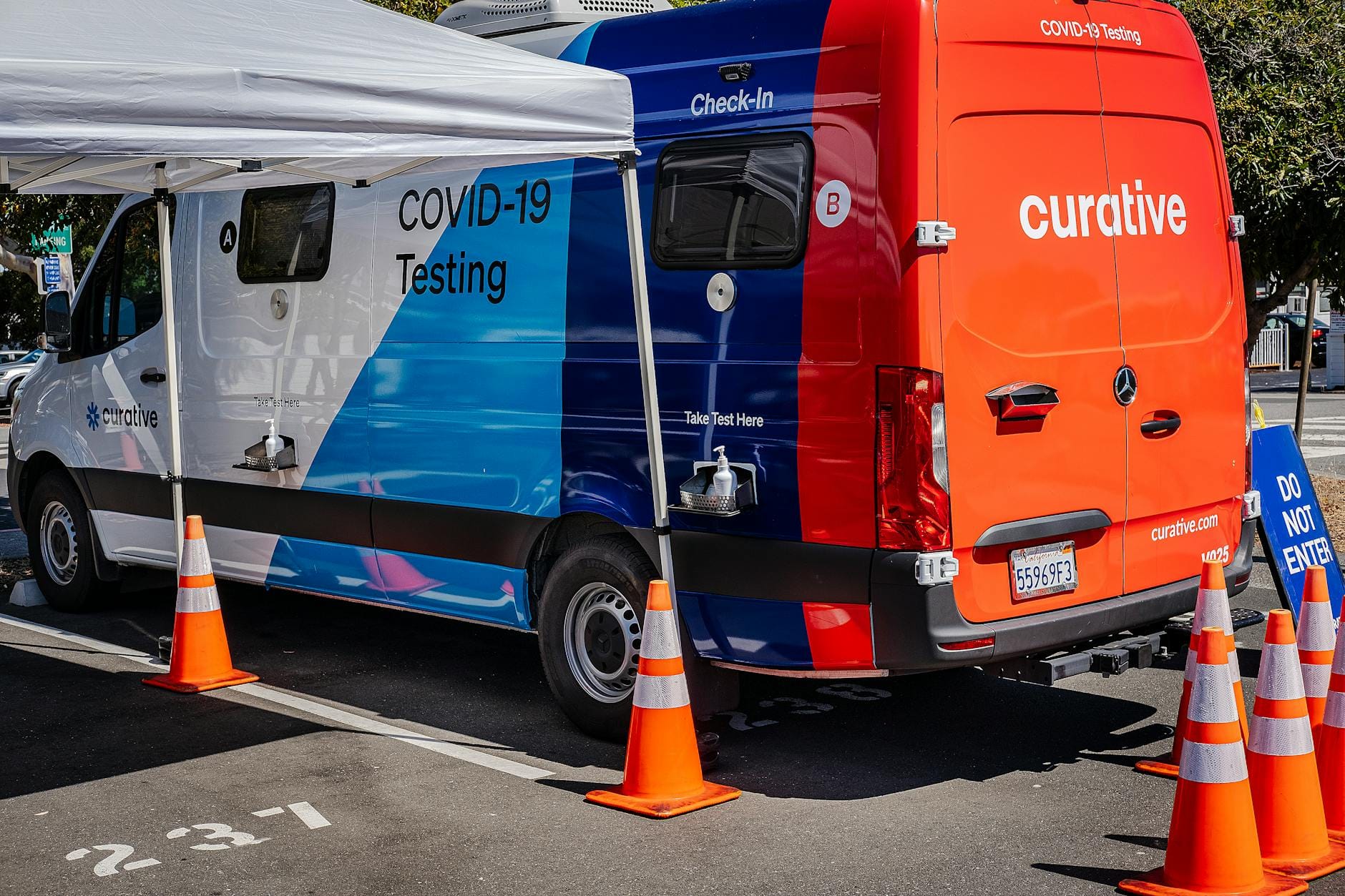 Mobilny punkt testów na COVID-19 z furgonetką i pachołkami na parkingu
