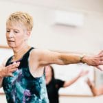 Starsza kobieta ćwicząca równowagę w domu podczas zajęć fitness