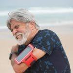 Starszy mężczyzna trzyma bolący bark podczas spaceru nad morzem