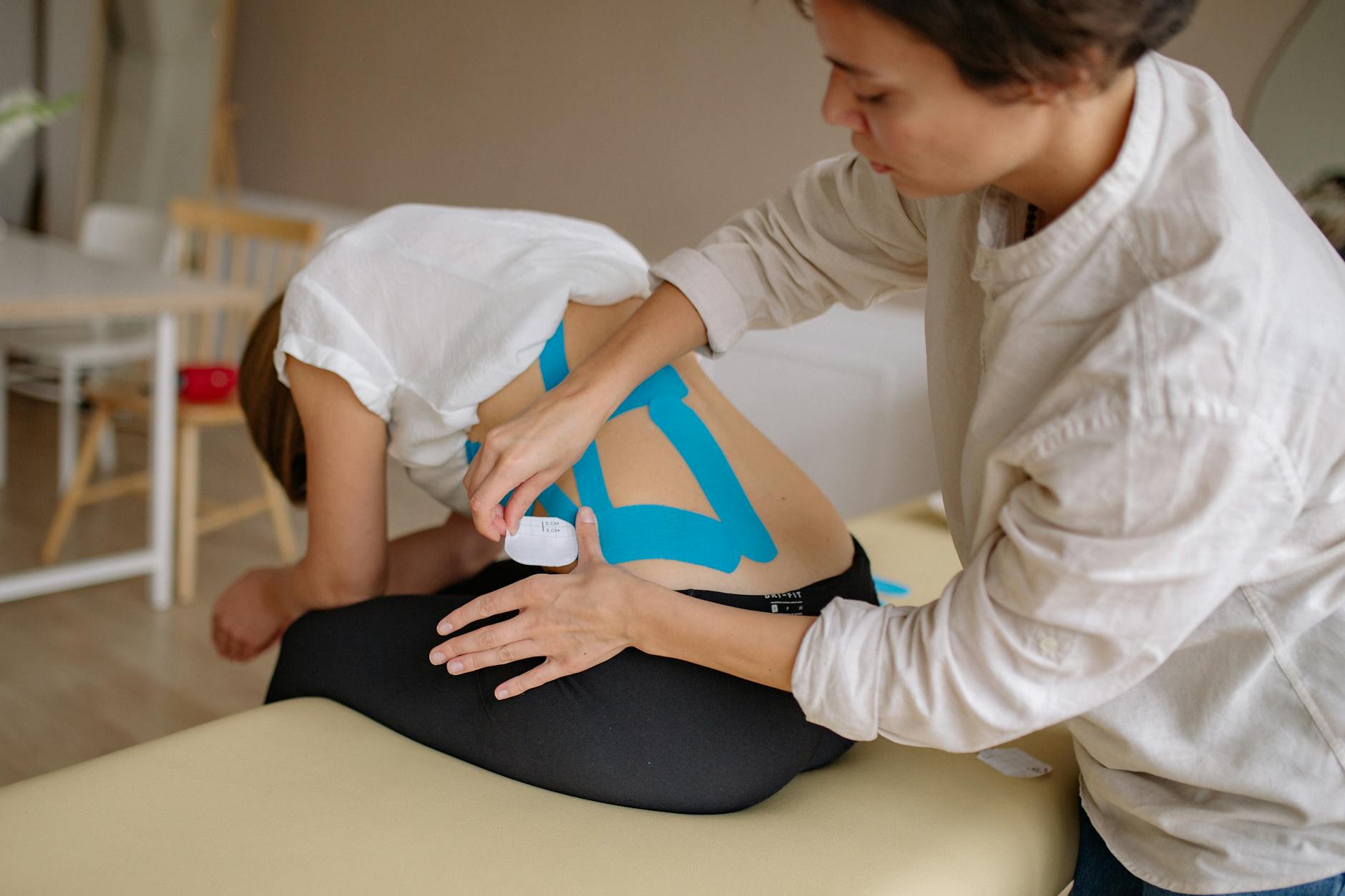Jak trenować stabilizację po epizodzie rwy kulszowej: zasady i bezpieczne ćwiczenia Fizjoterapeuta nakleja niebieskie taśmy kinesiotaping na plecy pacjenta
