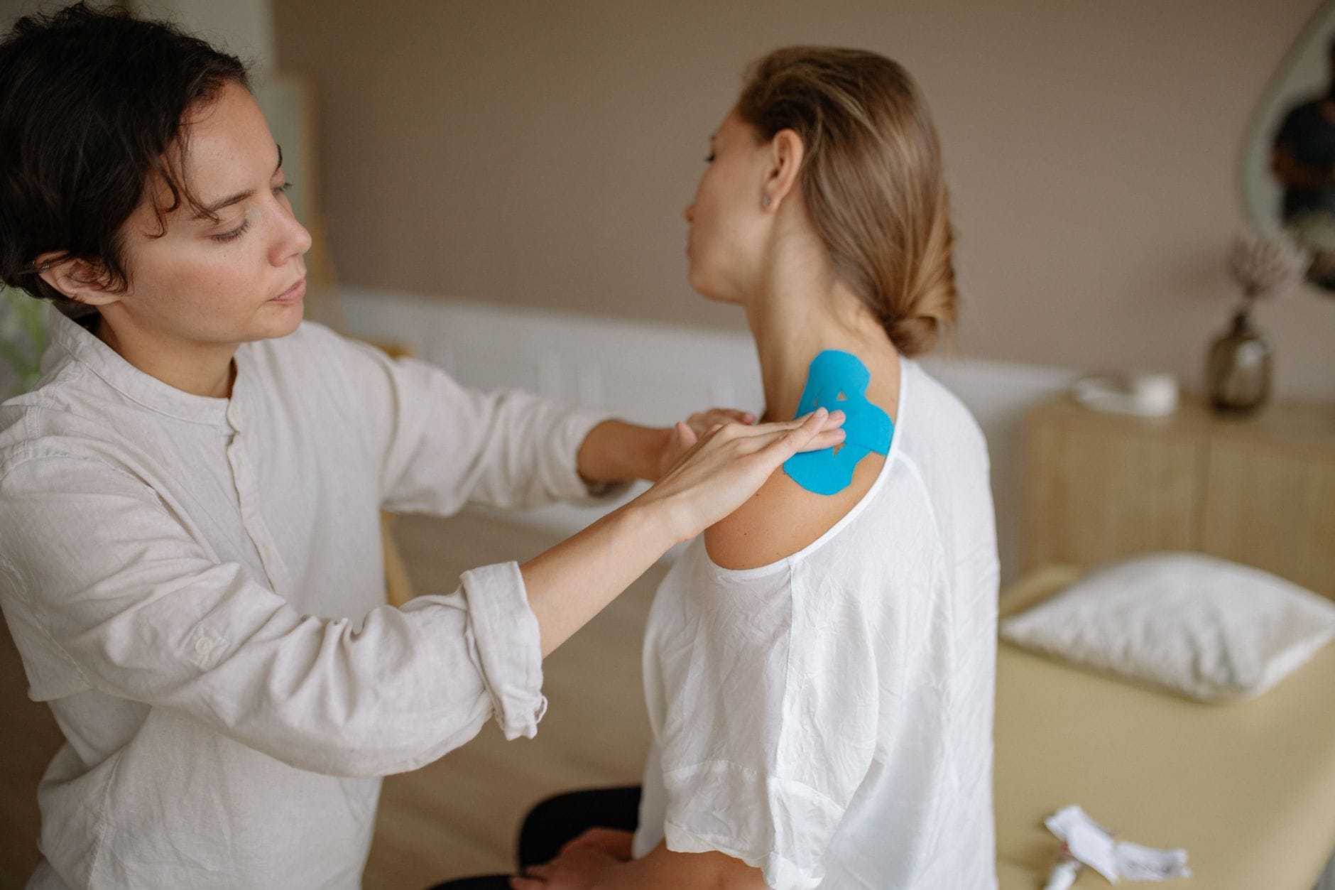 Fizjoterapeuta nakleja niebieskie plastry kinesio na bolący bark pacjenta