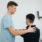 Fizjoterapeuta prowadzi terapię bolesnego barku pacjenta w gabinecie