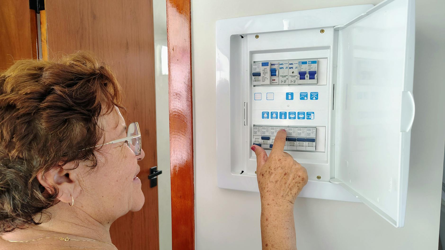 Starsza kobieta regulująca panel bezpieczników w domowej rozdzielnicy